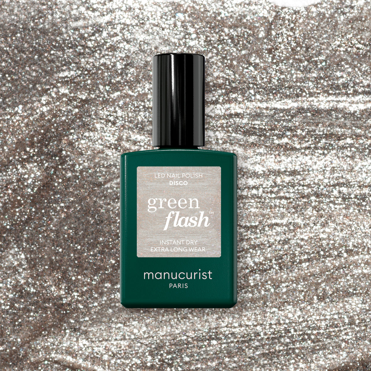 A bottle of Manucurist Disco gel polish stands out on a glittery silver background, its dark green bottle and black cap contrasting with the sparkling backdrop.