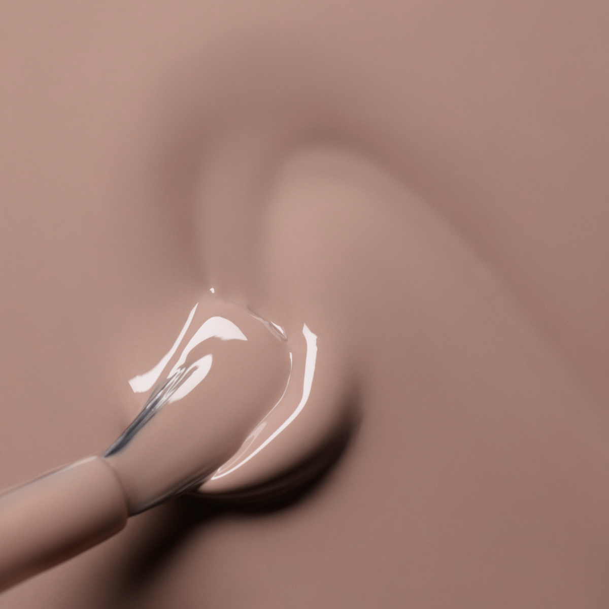 A close-up of a Manucurist Dove Beige brush spreading glossy pastel beige gel polish in a smooth swirl on a matching surface.