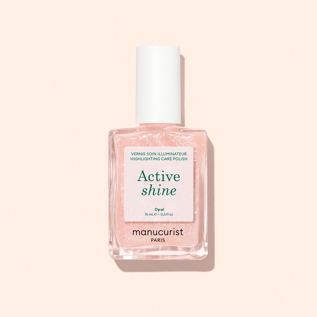 A clear glass bottle of Manucurist Active™ Shine Opal nail care polish with a white cap, photographed on a pale pink background. This plant-based formula features a label highlighting its repair and shine benefits, serving as an effective nail strengthener for healthier-looking nails.