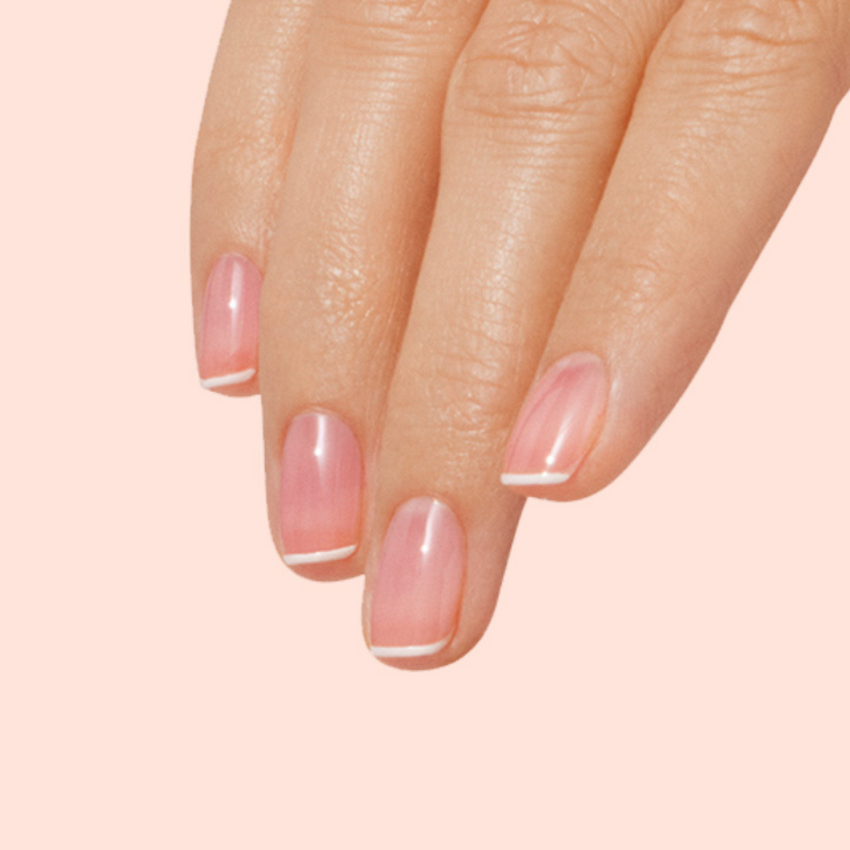 A hand with neatly manicured nails features a glossy minimalist French tip design on pale pink, created using the Manucurist French Manicure Glow kit.
