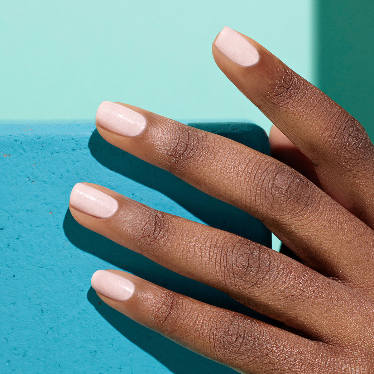 A hand with smooth brown skin and short, neatly manicured nails painted in Manucurist&