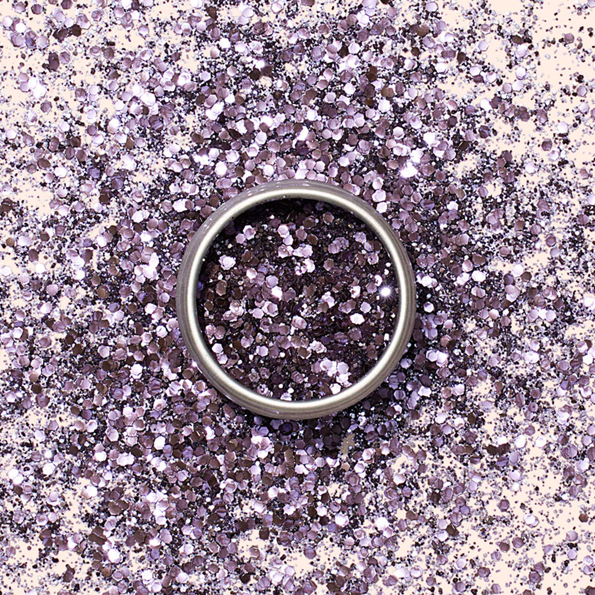 A silver ring sits on a surface covered in Manucurist Lilac biodegradable glitter, creating a sparkling and festive background reminiscent of elegant nail art.