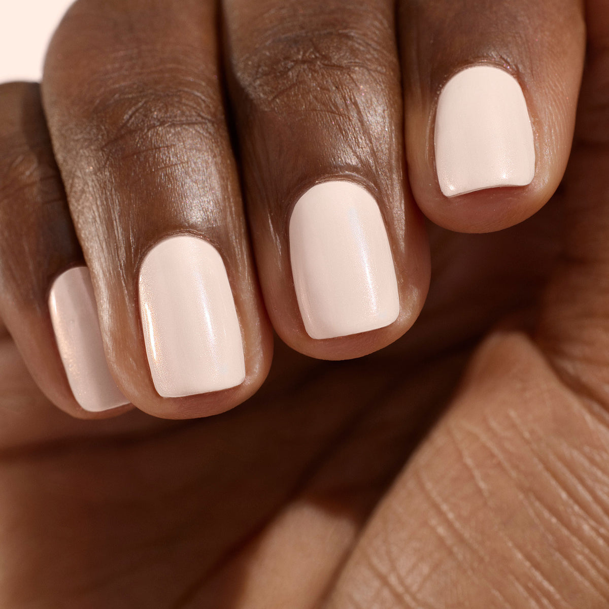 A close-up of a moisturized hand with short, evenly shaped nails showcases an ultra-glowy manicure in a pale nude or light pink shade using Manucurist’s The One  Only Duo.