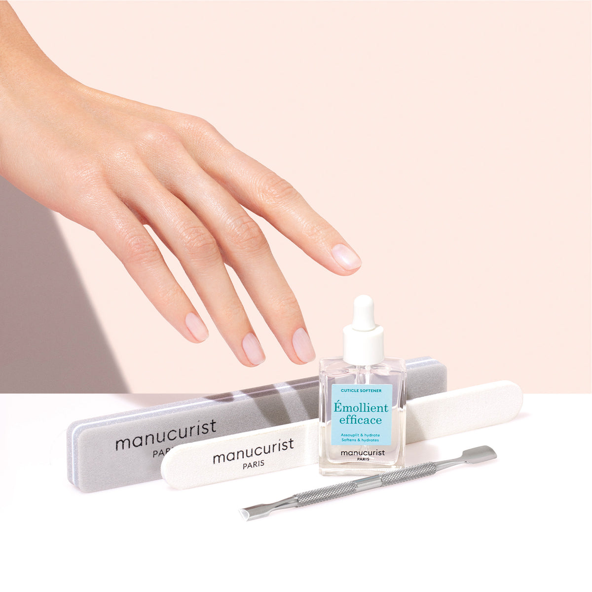 A hand with manicured nails hovers above the Manucurist Hydrating Cuticle Remover, two nail files, and a metal cuticle pusher, all neatly arranged on a light background.