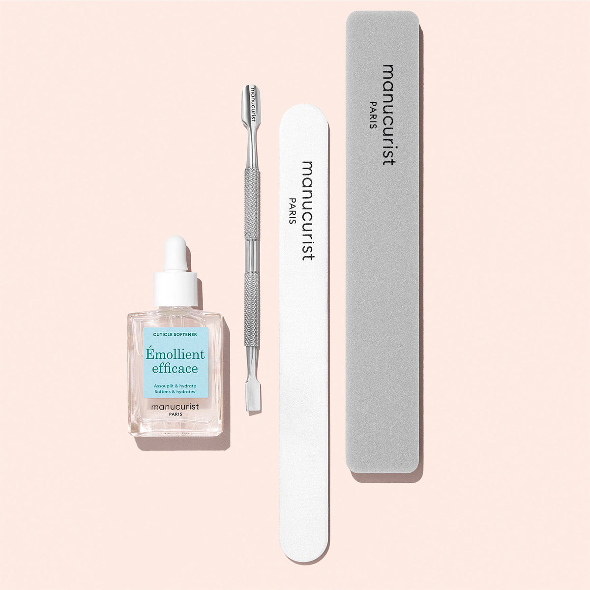 The Manucurist Hydrating Cuticle Remover set includes a cuticle softener, metal cuticle pusher, white nail file, and grey buffer, all arranged neatly on a pale pink background.