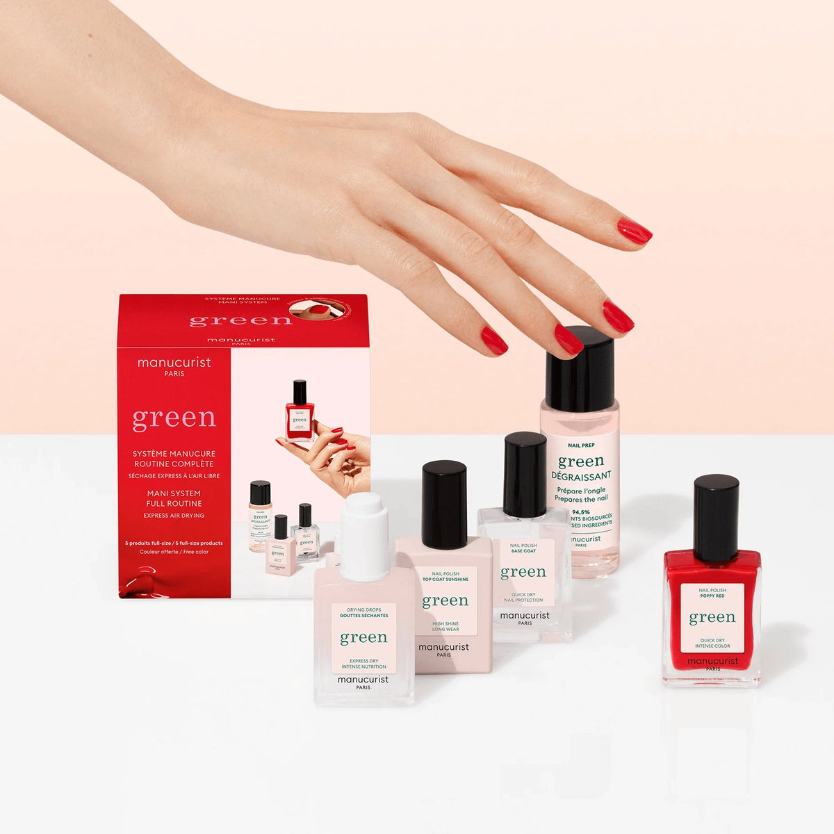 A hand with red polished nails hovers over the Manucurist Discovery Kit, a manicure set with gel effect nail polish and plant-based ingredients, displayed on a white surface against a pale pink background.
