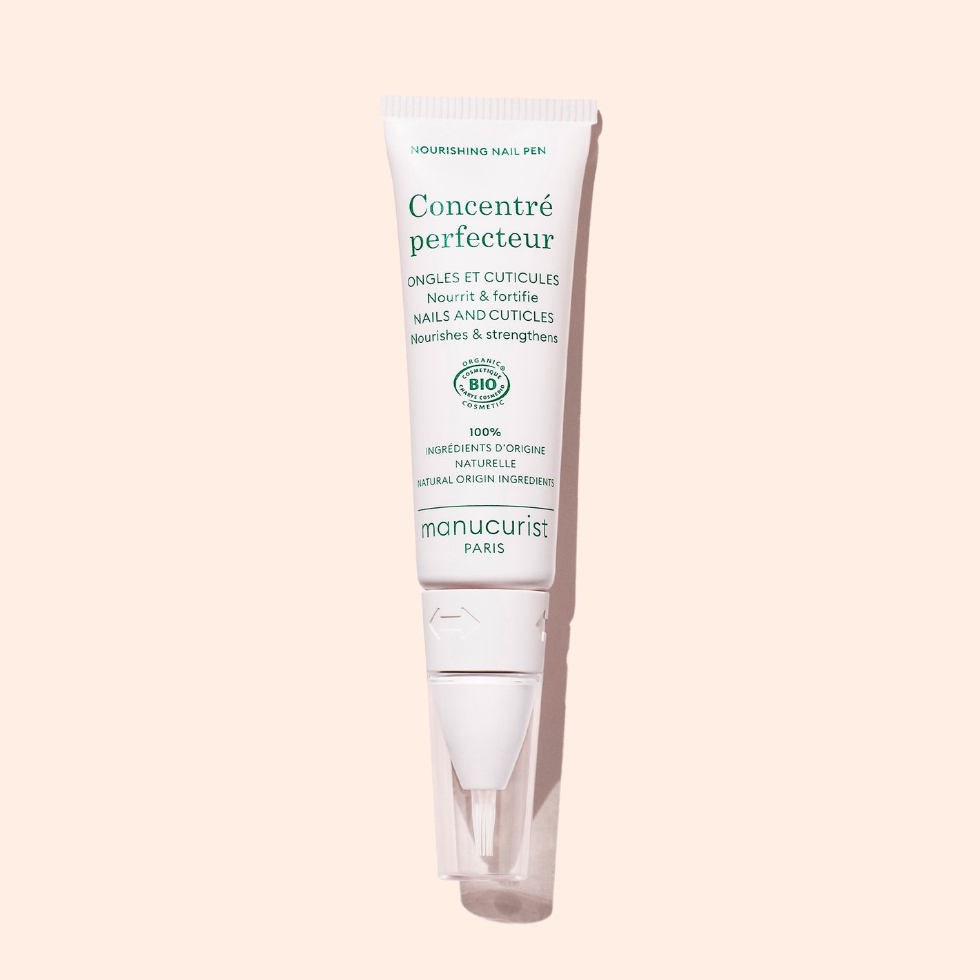 A white tube of Manucurist Nourishing Nail Pen - Cosmos Organic with green text stands upright on a light pink background. Ideal for cuticle care, the tube has a clear cap and angled applicator tip.