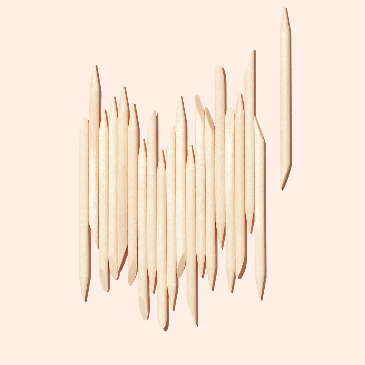 A set of Manucurist-test Wooden cuticle stick x20 neatly arranged vertically on a pale pink background, with one stick positioned separately to the right.
