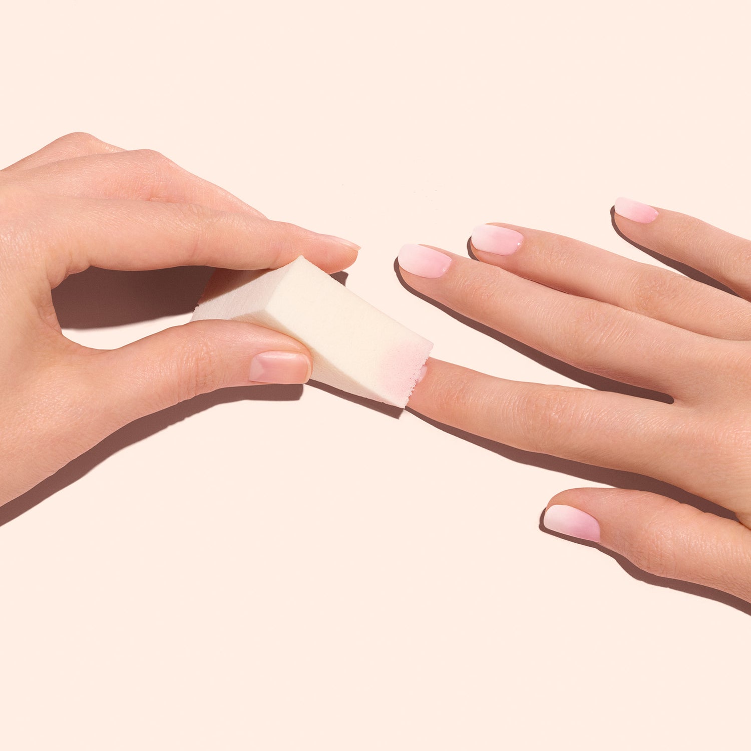A hand uses a Manucurist Nail Art Sponge from the set of four to apply pink polish and create soft gradient nails, all displayed on a light pink background.