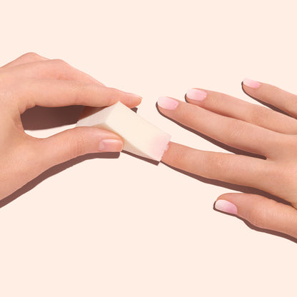 A hand uses a Manucurist Nail Art Sponge from the set of four to apply pink polish and create soft gradient nails, all displayed on a light pink background.