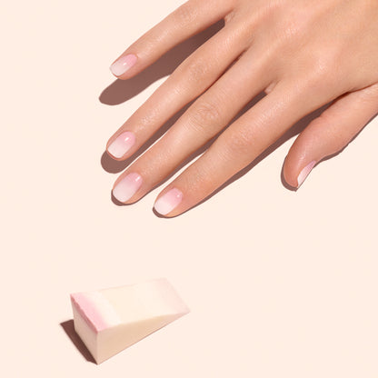A hand with natural pink and white ombre nails rests on a peach background. Nearby are Manucurist’s Nail Art Sponges (x4), perfect for creating seamless aura nail gradients.