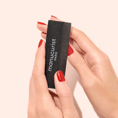 Hands with red nail polish holding a black Manucurist Flash Removal Block.