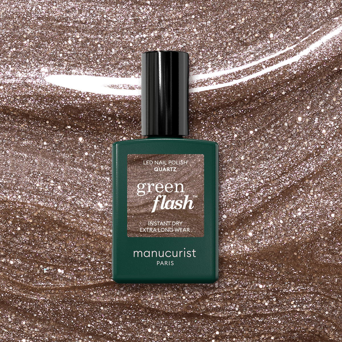 A bottle of Manucurist Quartz nail polish rests on a glittery brown surface. The chestnut brown shade features a shimmery, metallic finish.