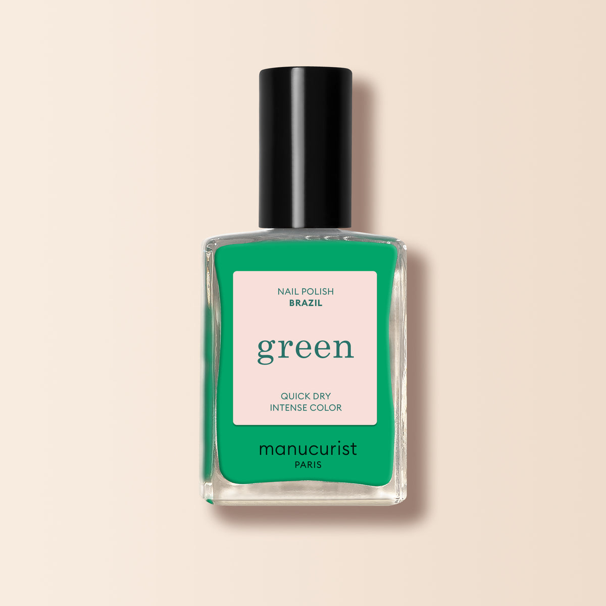 A bottle of Manucurist Brazil nail polish from the Green™ range, featuring intense electric green color and a black cap, is photographed against a pale beige background. The label shows green and pink colors with text.