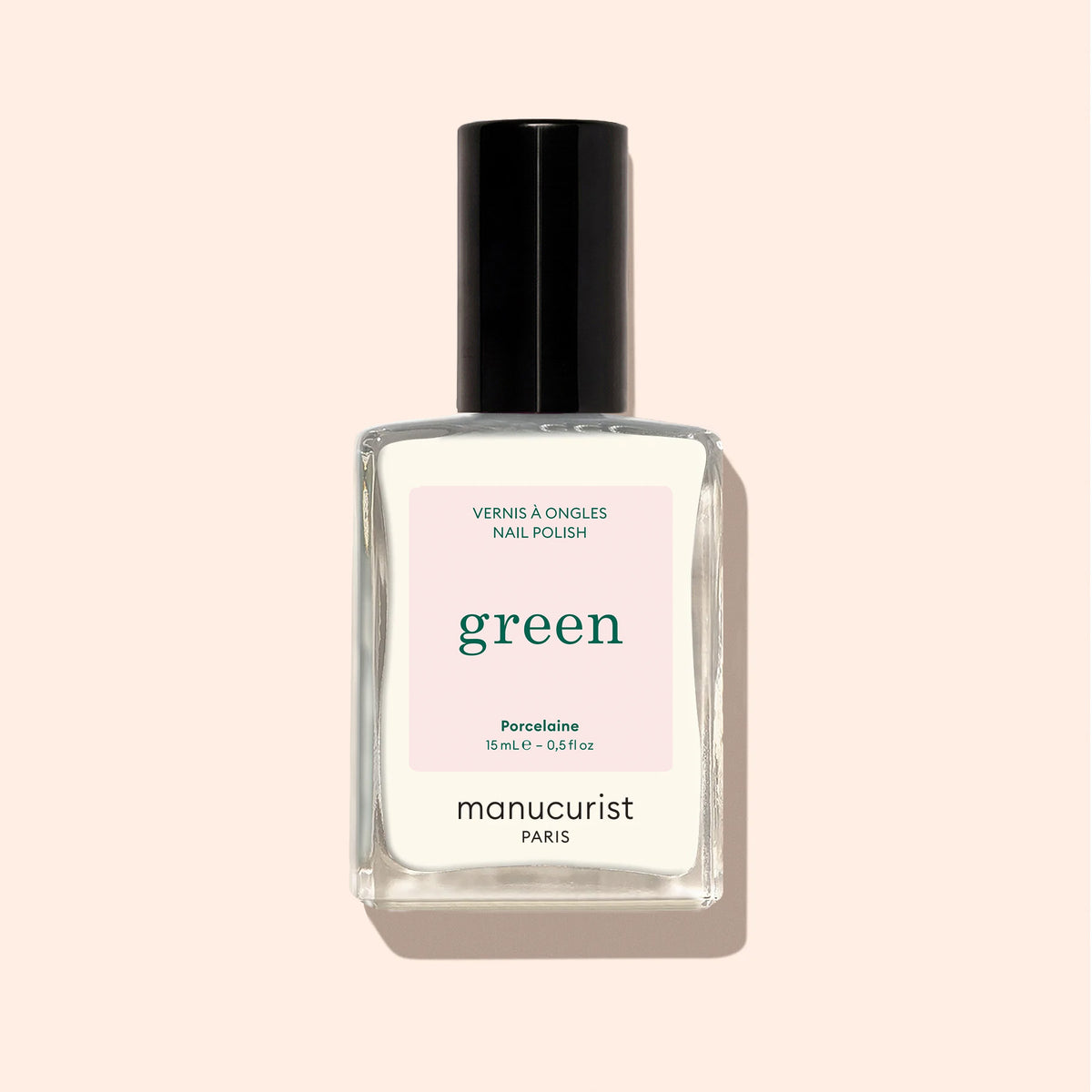 A bottle of Manucurist nail polish in Porcelaine, with a black cap, clear rectangular glass, and minimalist white label, shown on a pale beige background.
