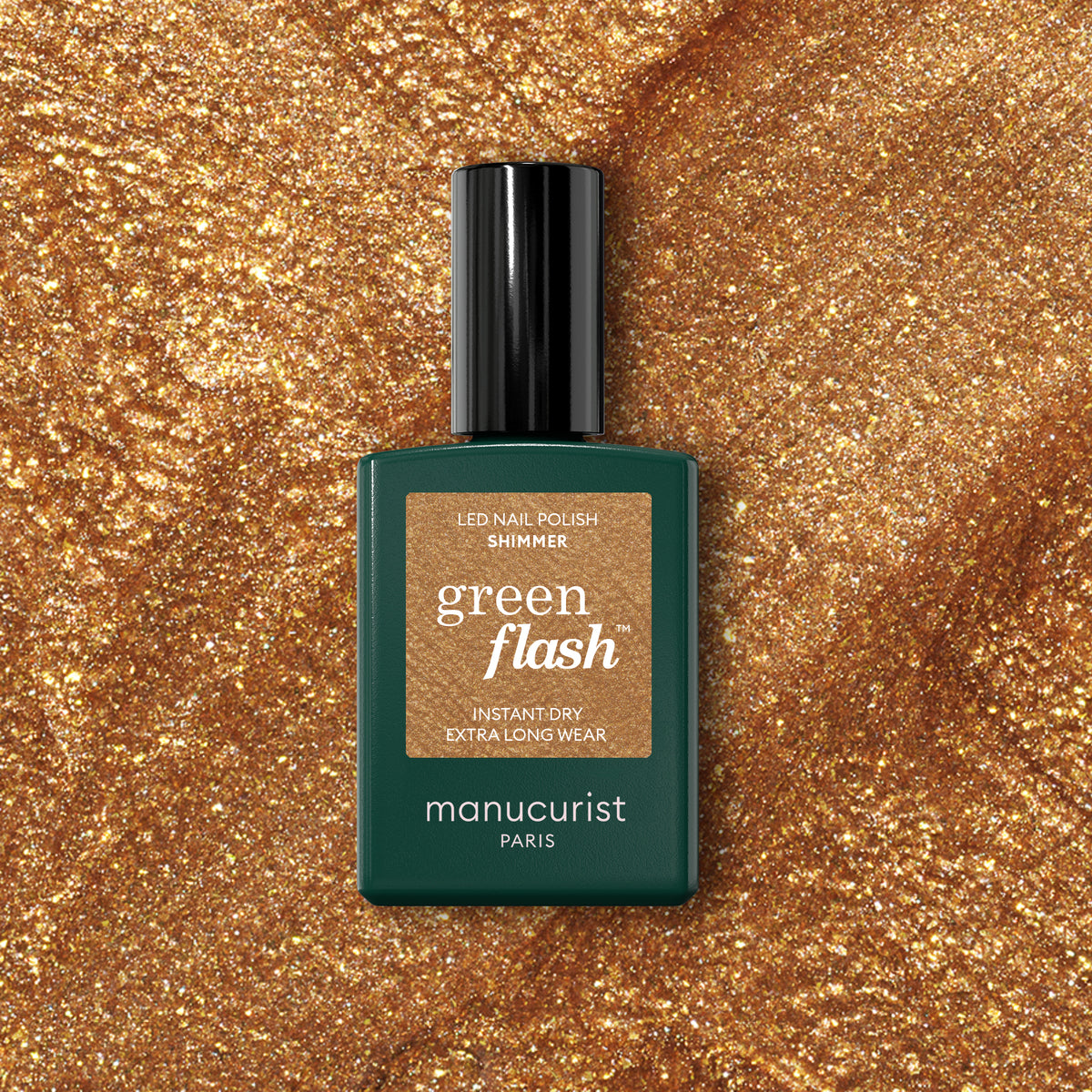 A bottle of Manucurist Shimmer gel polish in a dark green container with a gold label sits on a sparkling gold textured background.