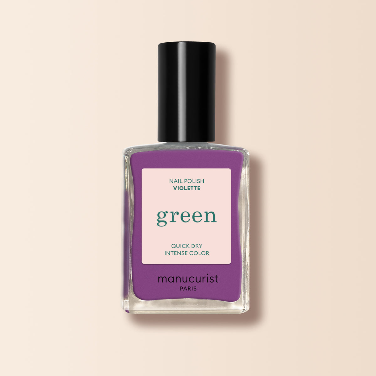 A bottle of Manucurist nail polish in the shade Violette shows a retro purple color through clear glass. It features a black cap and a label reading “green, quick dry intense color” on a light beige background.
