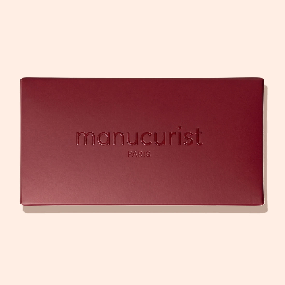 A closed rectangular Burgundy Holiday Rainbow Box by Manucurist, featuring the brand name embossed on the lid, set against a light beige background.