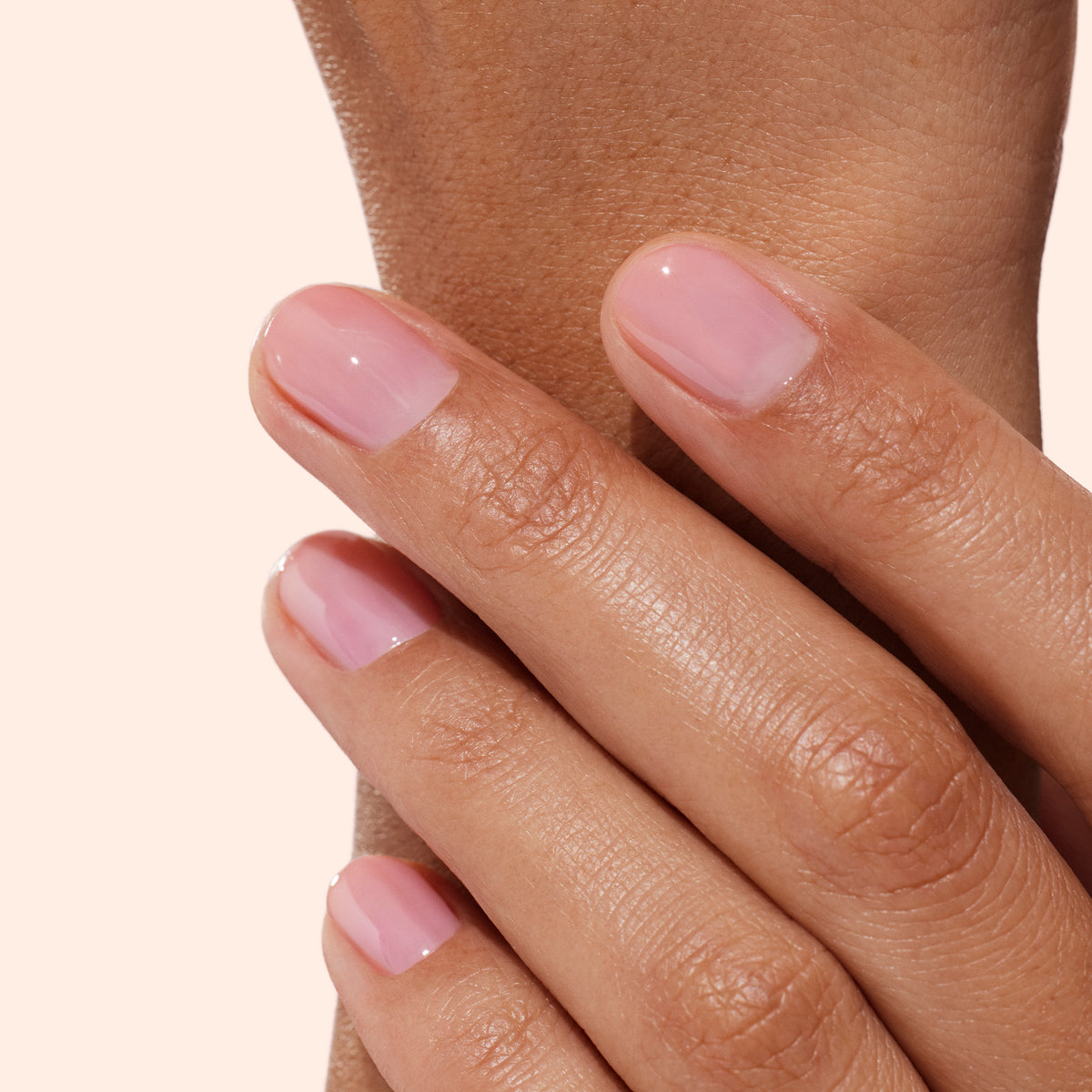 A close-up of a hand with short, neatly manicured nails painted in the glossy, light pink shade of Manucurist’s Active™ Glow Blueberry, showcasing radiant shine and nail nourishment, resting gently on the wrist of the opposite hand against a light background.