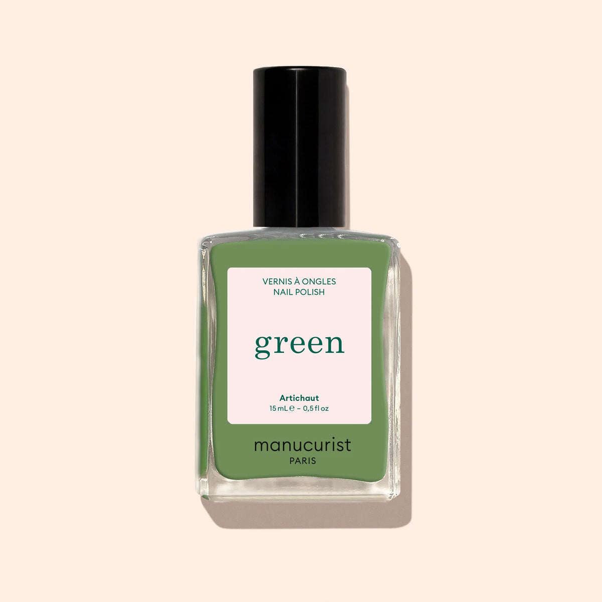A bottle of Manucurist Artichoke nail polish from the Green™ range, with a black cap and herbal green shade, stands upright against a light beige background.