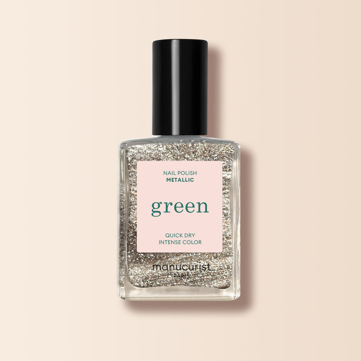 A bottle of Manucurist Metallic nail polish with metallic gold glitter, a black cap, and a pale pink label stating “Nail Polish Metallic, green, Quick Dry Intense Color,” displayed on a neutral background.