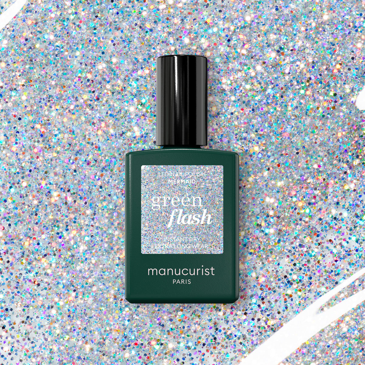 A bottle of Manucurist Green Flash gel polish in the shade "Mermaid" sits on a sparkling, multicolored glitter background. The dark green bottle features a holographic label and a sleek black cap.