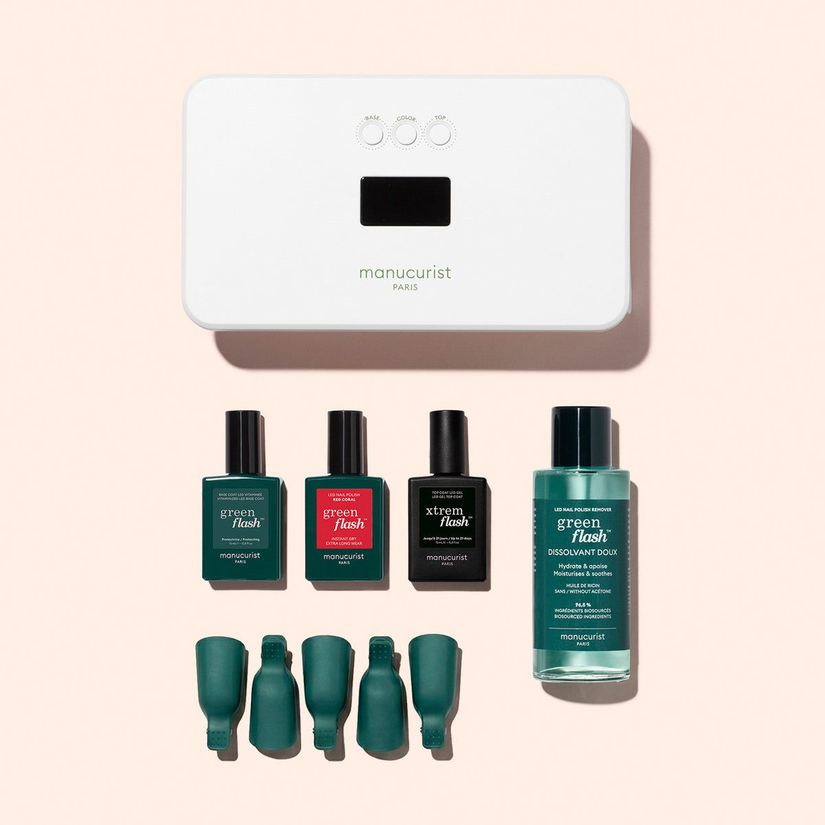 The Manucurist Discovery Kit includes a white UV lamp, three bottles of long-lasting nail polish, a remover bottle, and four green finger clips—beautifully arranged on a peach background—to provide everything you need for an ultra-glossy manicure at home.