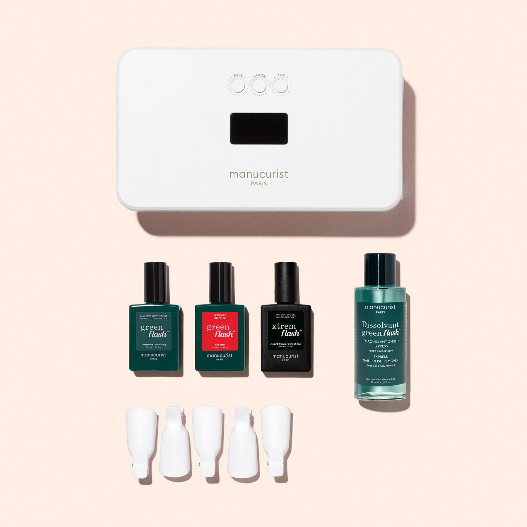 The Manucurist Discovery Kit includes a white LED nail lamp, three polishes (with vitaminized base coat), remover, and four white caps—everything you need for an ultra-glossy manicure, arranged on a chic pink background.