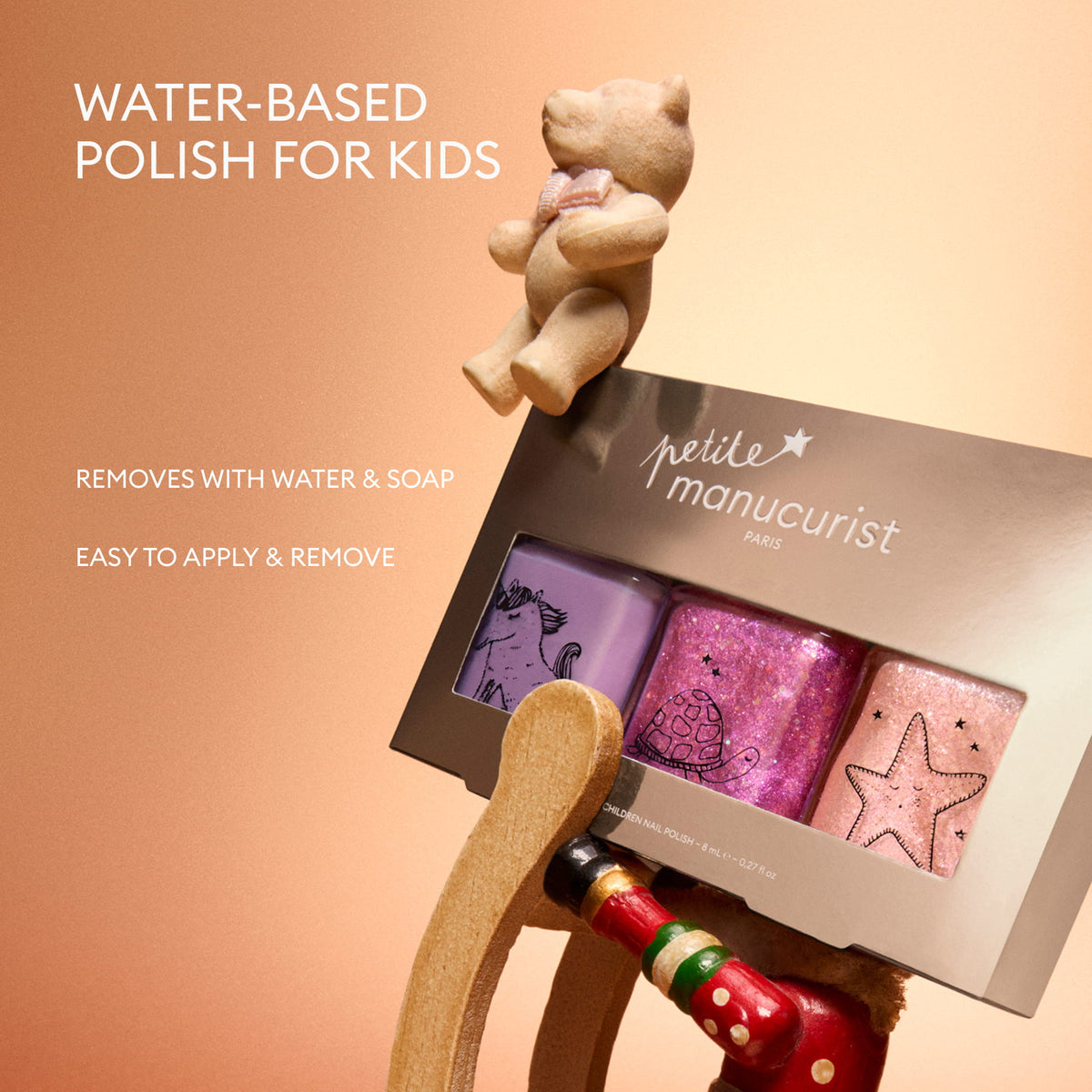 A wooden rocking horse displays the Manucurist Petite Manucurist Trio: a set of children’s nail polishes in purple, pink, and glitter shades. Text reads: Water-based polish for kids—removes easily with water and soap. Made from natural origin ingredients, easy to apply and remove, perfect as a holiday gift.