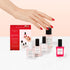 A hand with red nails reaches for manicure products, including the Manucurist Discovery Kit - Jelly Nail Polish, on a pale pink and white background.