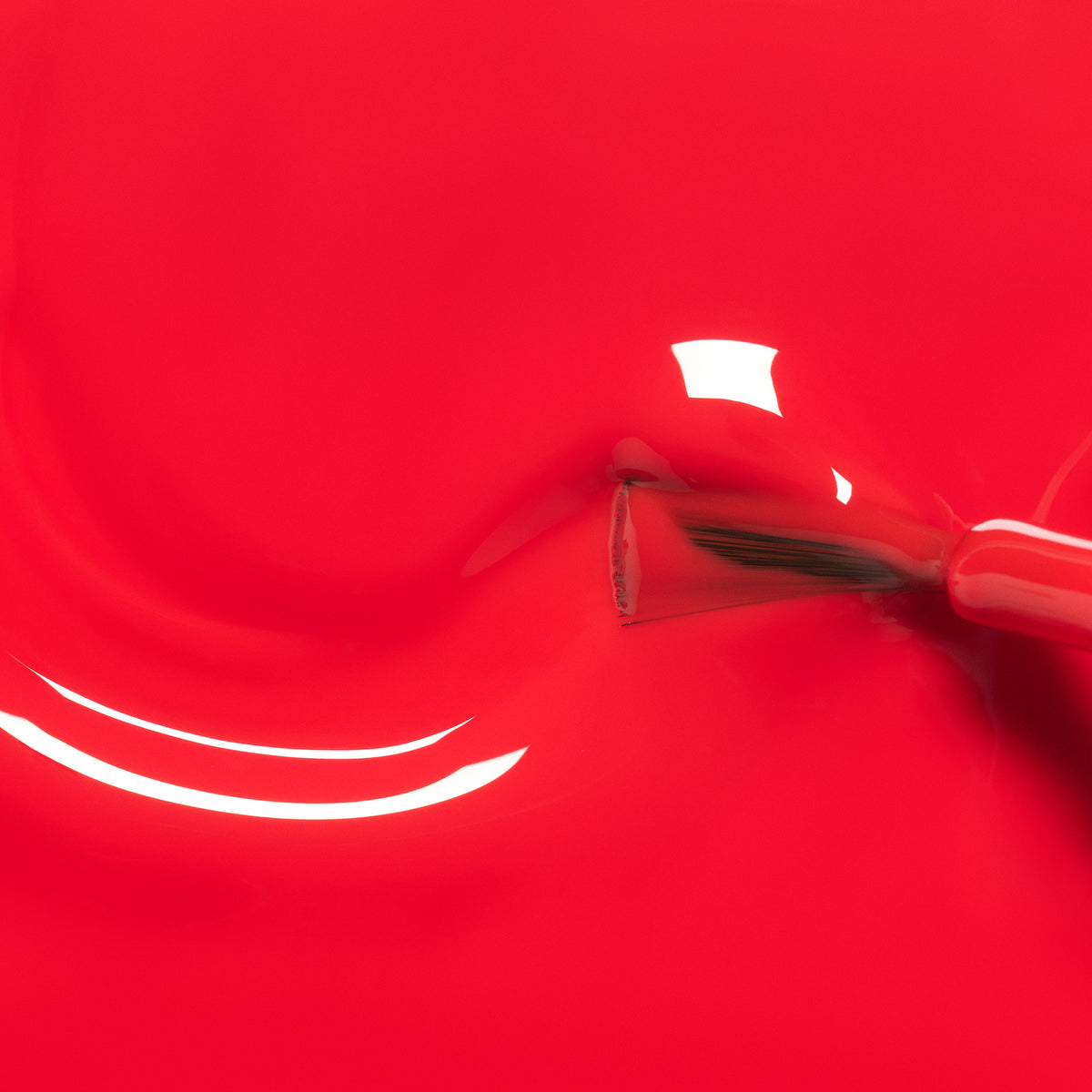 A close-up of a nail polish brush spreading Lucette the Warbler by Manucurist—a bright, kid-friendly red that creates smooth, glossy swirls with fun and safe color.