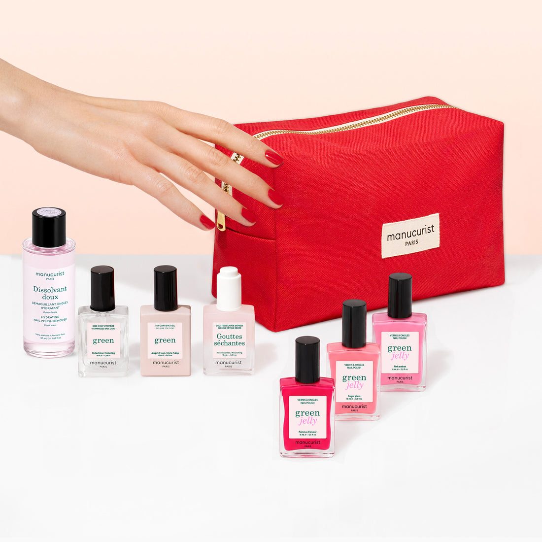 A hand with red nail polish holds a vibrant red cosmetic bag from Manucurist. In front, a green manicure kit from the Manucurist Starter Kit - Jelly Nail Polish collection stands out among six bottles of gel-effect nail polish and a bottle of nail polish remover, all arranged neatly on a light surface.
