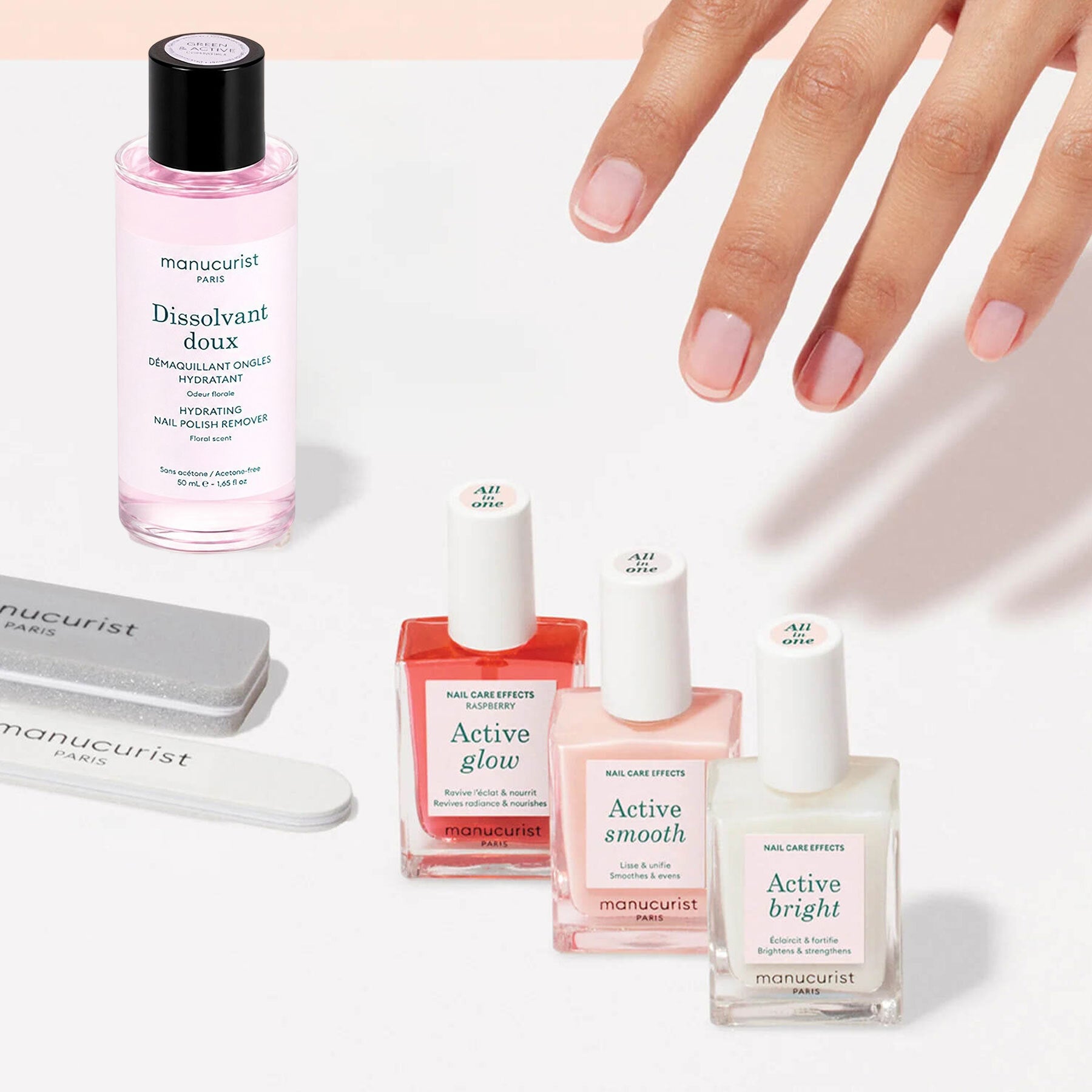 A manicured hand is displayed alongside the Manucurist Active™ Manicure Kit, featuring nail polish remover, three nail polishes, and nail files—all neatly arranged on a white surface. These essentials from Manucurist provide the perfect start to your flawless manicure routine.