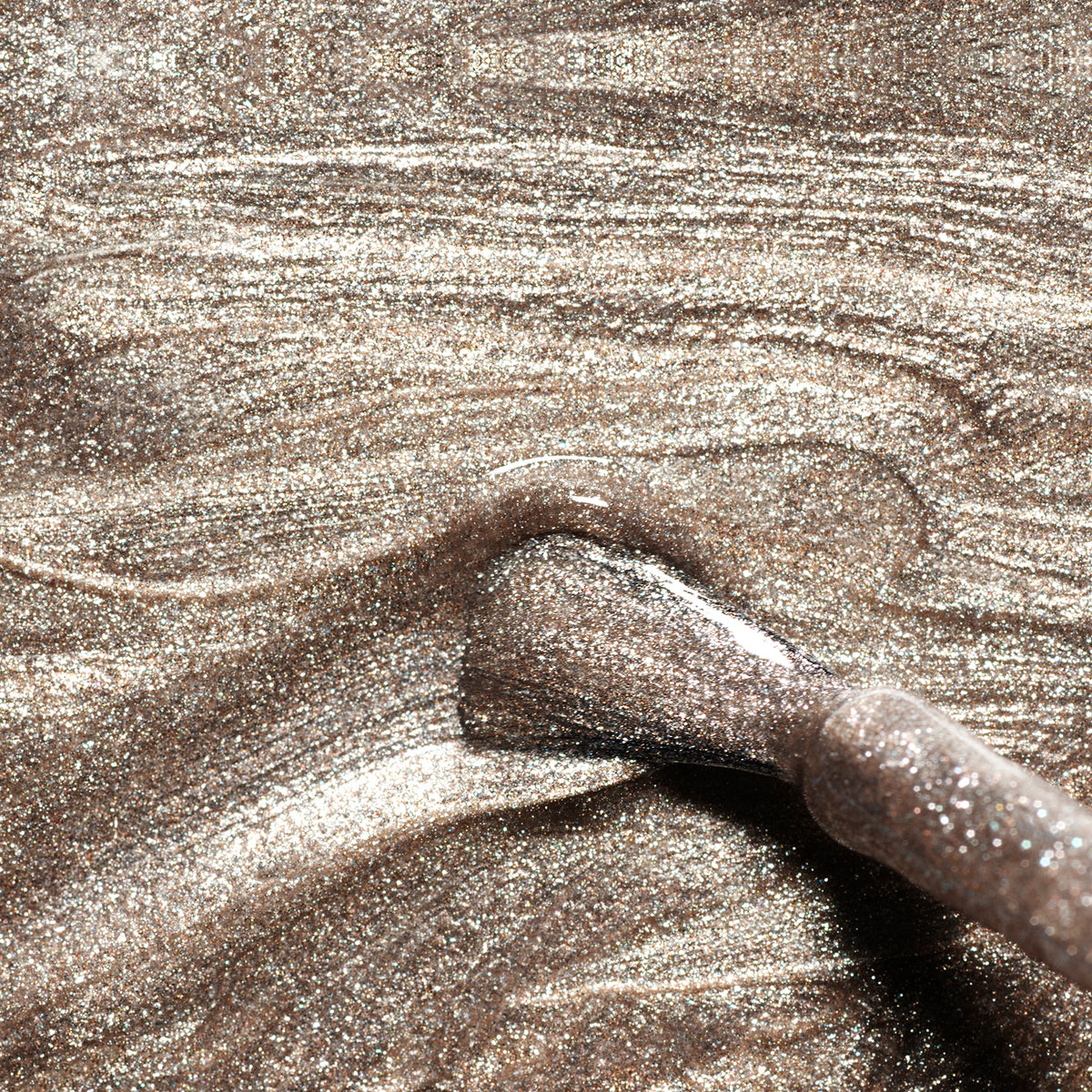 Close-up of a Manucurist Spice Lover brush applying shimmery metallic silver nail polish, spreading sparkling color in swirling patterns across a smooth surface with expert nail art tools.