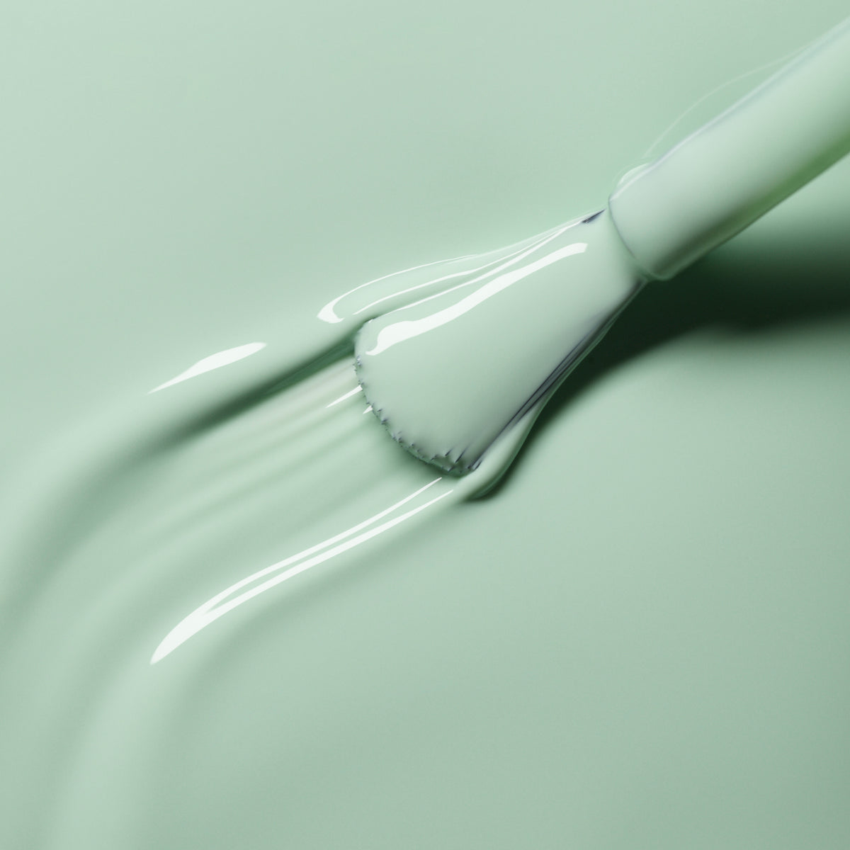 A close-up of a brush spreading smooth, light green Retro rainbow by Manucurist on a surface, creating glossy, textured strokes.