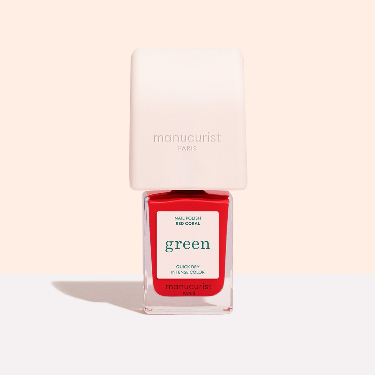 A bottle of Manucurist Mani Helper nail polish in Red Coral, with a white square cap and clear glass showing the red polish, ideal for a perfect manicure, photographed against a light background.