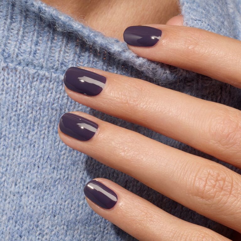 A hand with neatly manicured nails painted in Manucurist’s Queen of Night, a glossy purple polish, rests on a light blue knitted sweater.