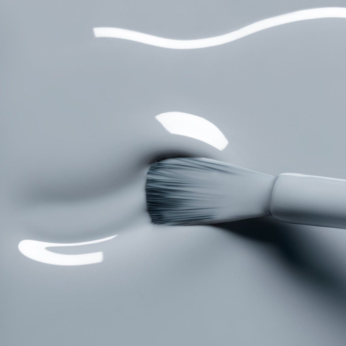 A close-up of a brush applying Manucurist’s Mist Grey gel polish—a glossy, muted blue—on a smooth surface, with light reflecting on the liquid.