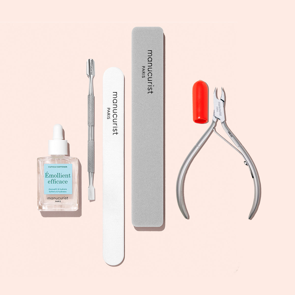 The Manucurist Super Nail Prep Set features cuticle oil with dropper, a metal pusher, emery board, buffer block, and nail clippers with a red cap—neatly arranged on a pale pink background.