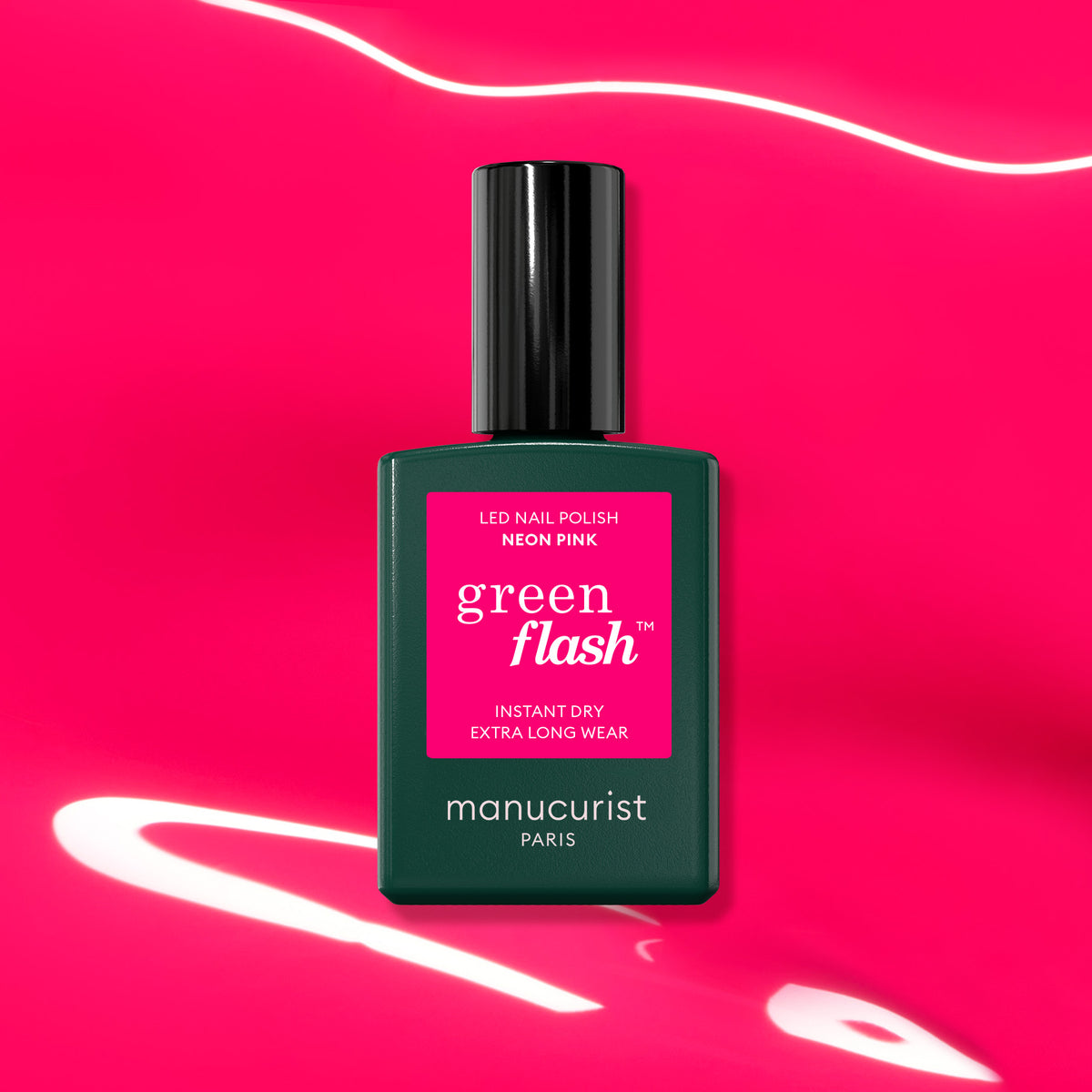 A bottle of Manucurist Neon Pink gel polish stands against a vibrant pink background with white light streaks. The dark green bottle and bold pink label emphasize this perfect summer shade.