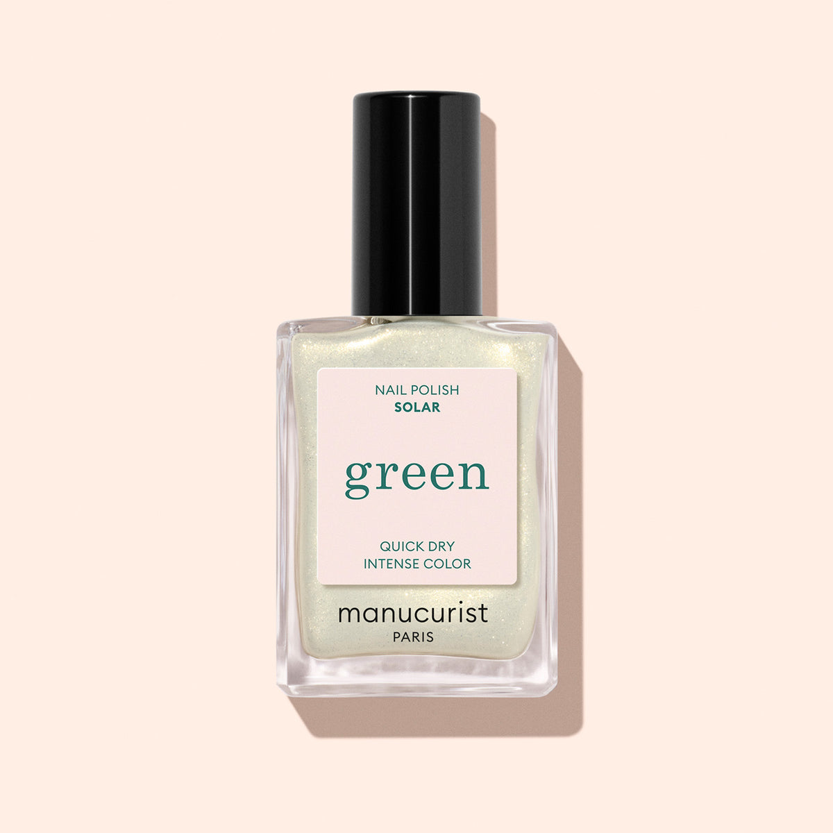 A bottle of Manucurist Solar nail polish, a light shimmery shade with golden highlights and a black cap, is displayed against a pale beige background.