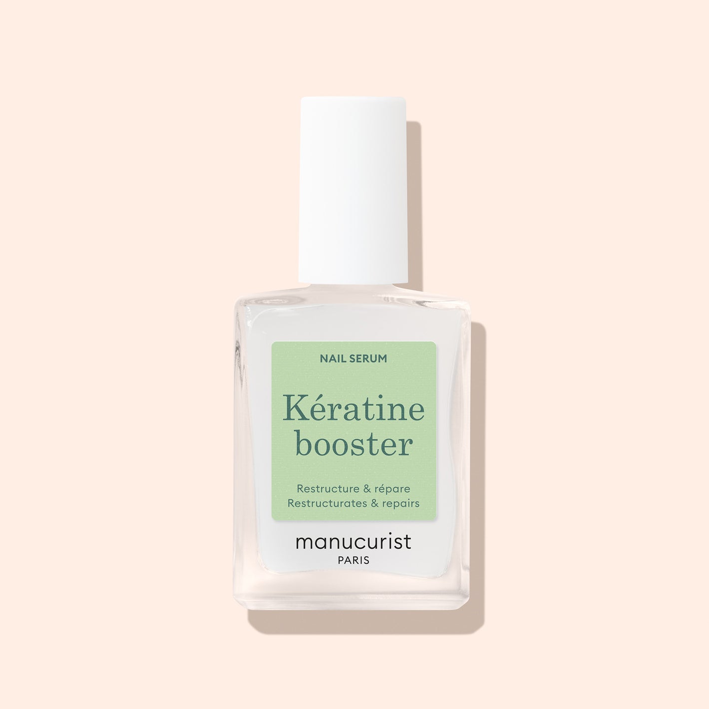 A clear glass bottle of Manucurist Nail Strengthening Serum with a white cap sits on a light beige background. Its light green label displays product details in French and English, highlighting its nail-strengthening properties.