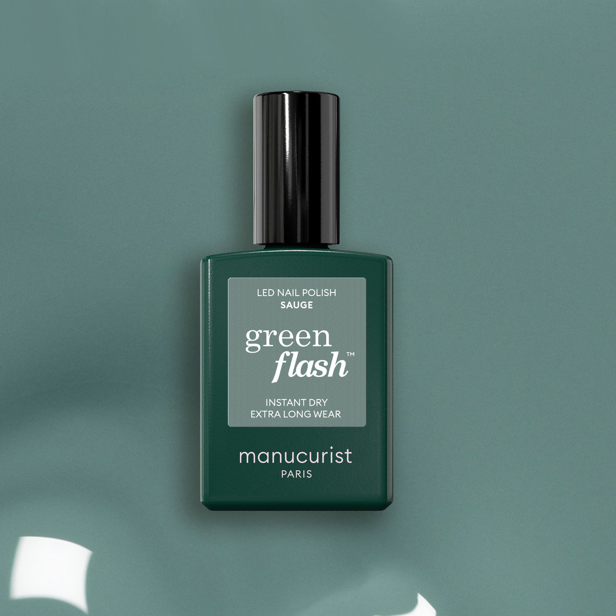 A bottle of Manucurist Sage LED nail polish, a deep sage green shade with a black cap, is displayed on a matching green surface with subtle light reflections.