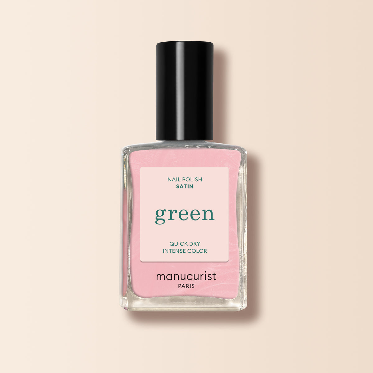 A bottle of Manucurist Satin nail polish in pale pink, featuring a pink label and black cap, is displayed on a light beige background. The label highlights its satin finish, quick-dry formula, and intense color.