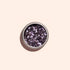 Manucurist’s Lilac biodegradable glitter is a small, round pot of chunky metallic purple plant-based glitter on a light beige surface—perfect for eco-friendly nail art fans.