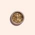 A round container of Manucurist Gold biodegradable glitter, ideal for nail art, is shown from above on a light beige background.