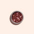A small round container of Manucurist Pink Quartz biodegradable glitter sits on a light beige background. Ideal for nail art or mixing into gel polish, the chunky pink glitter sparkles beautifully in the light.