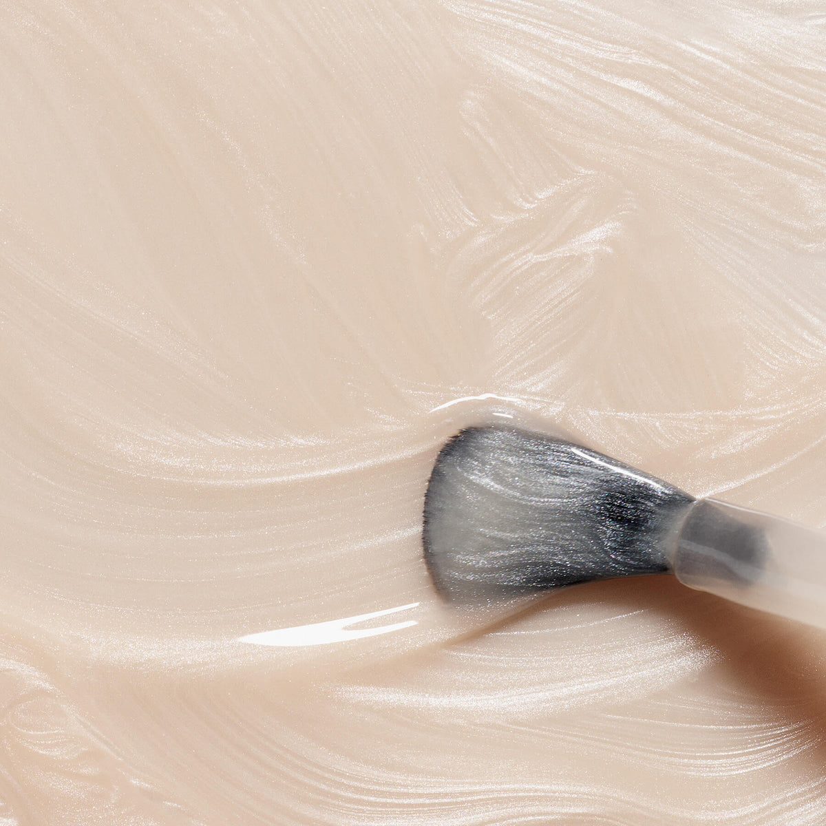 A close-up of a makeup brush spreading Manucurist’s Pearlescent, a creamy beige cosmetic with a smooth, shimmery texture.