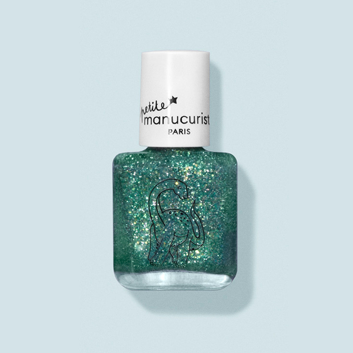 A bottle of Manucurist kids nail polish in green glitter, named Marius the Diplodocus, features a white cap and a black dinosaur outline on the label. Made with natural ingredients, it is displayed against a pale blue background.
