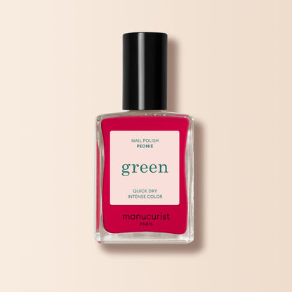 A bottle of Manucurist-test nail polish in the pink shade Peonie OLD, featuring a black cap, is photographed against a light beige background.
